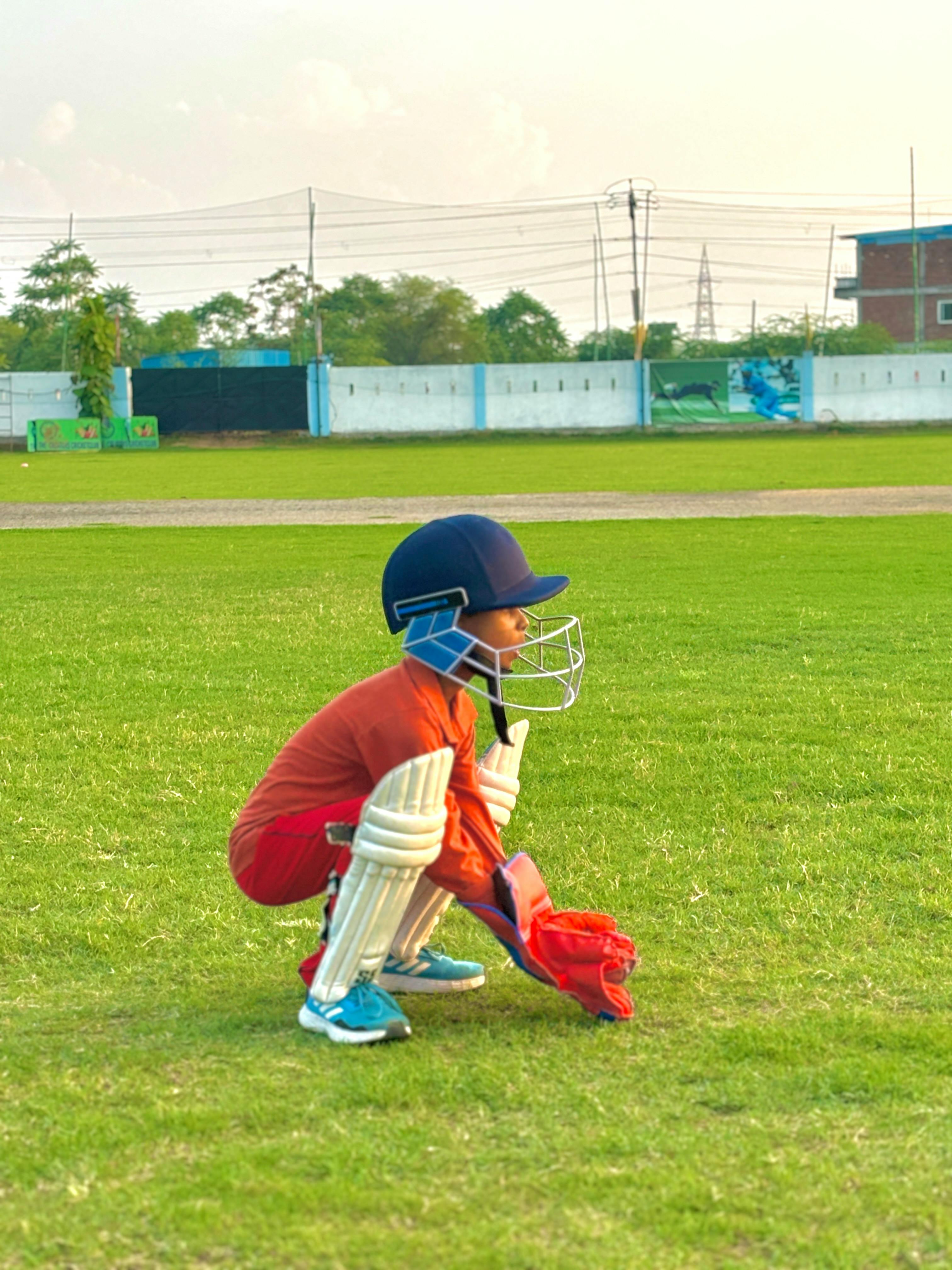 Young cricketer in gear crouching on a green field, ready for action.