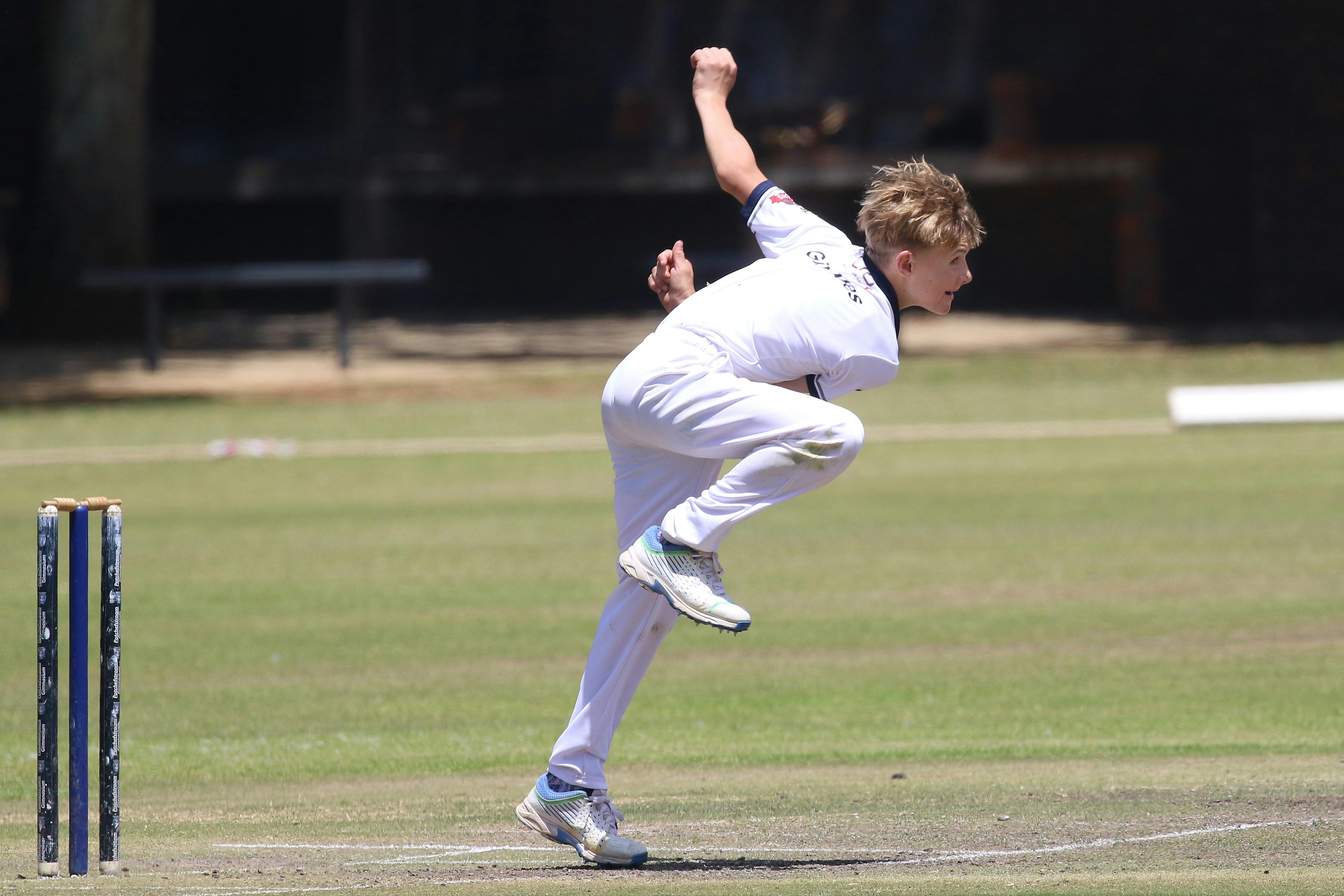 Young cricketer in action on a sunny day, captured mid-bowling with intense focus.